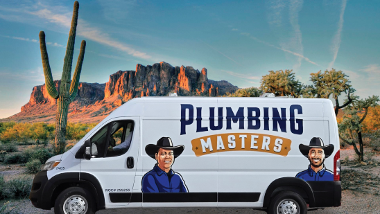 White van with “Plumbing Masters” and illustrations of two men in cowboy hats, parked in a desert landscape with cacti and mountains in the background.